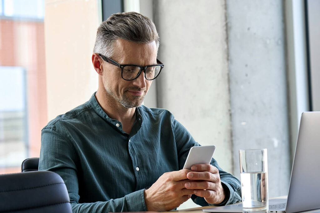 Middle aged man with glasses looking at smartphone in office.