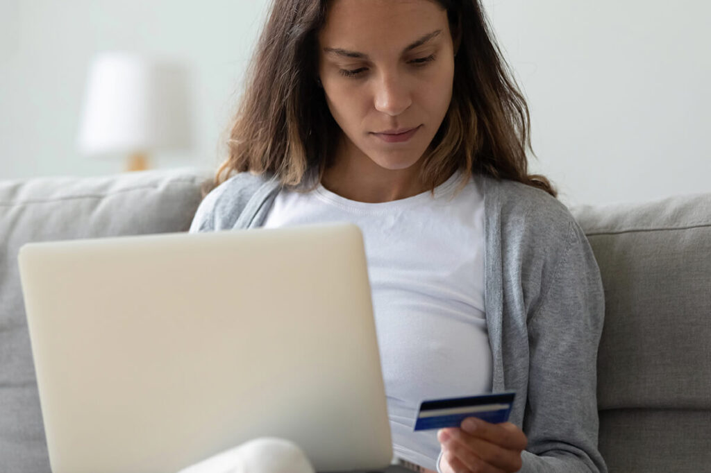 Person sitting on couch with laptop on lap looking at credit card information.